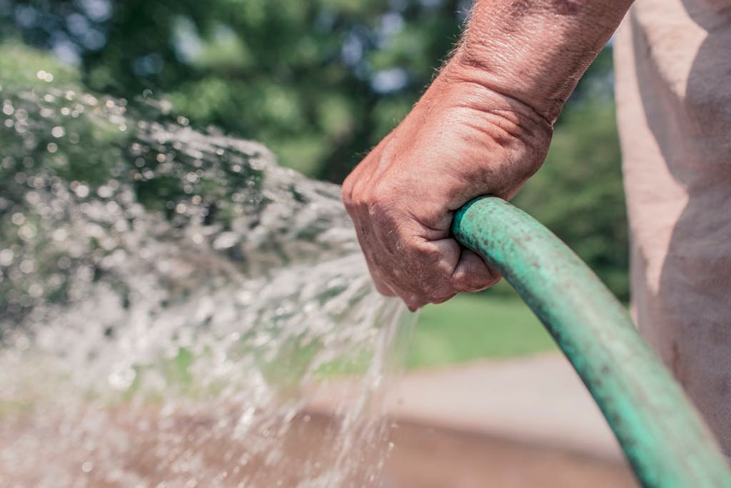 A photo of a person holding a green garden hose. Now Air Conditioning | Why Clean Outdoor Air Conditioner Unit?